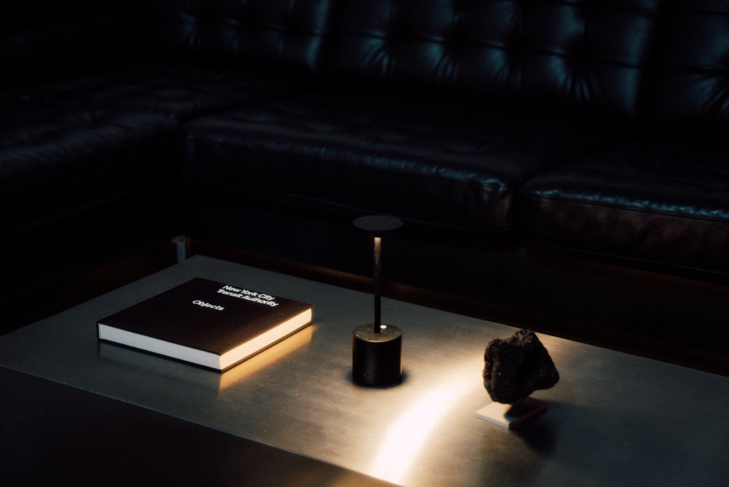 A steel table under a single lamp — a book, and a mounted rock.