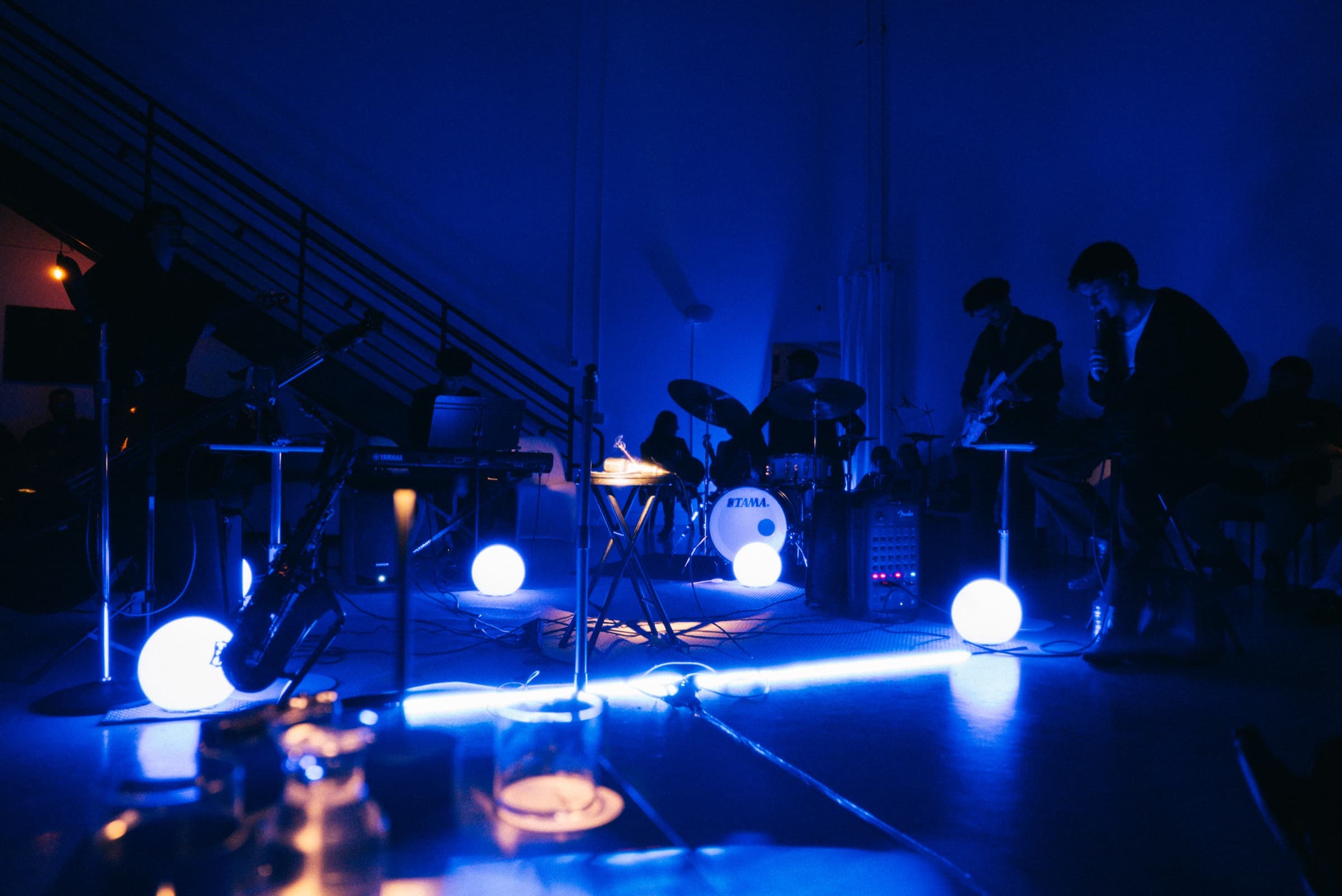 The same set under cobalt wash, the band in silhouette behind lit globes.